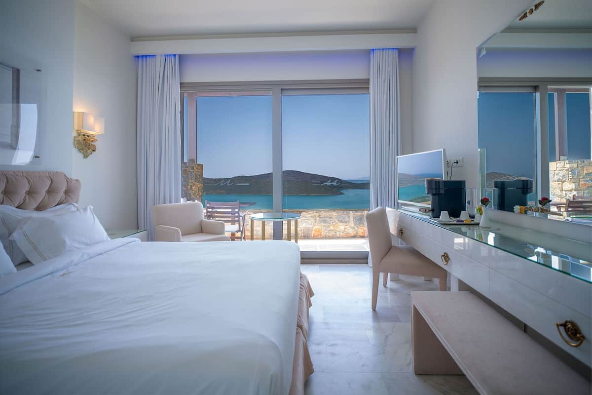Une chambre d’hôtel avec un grand lit, un bureau, une chaise et une vue sur la mer.