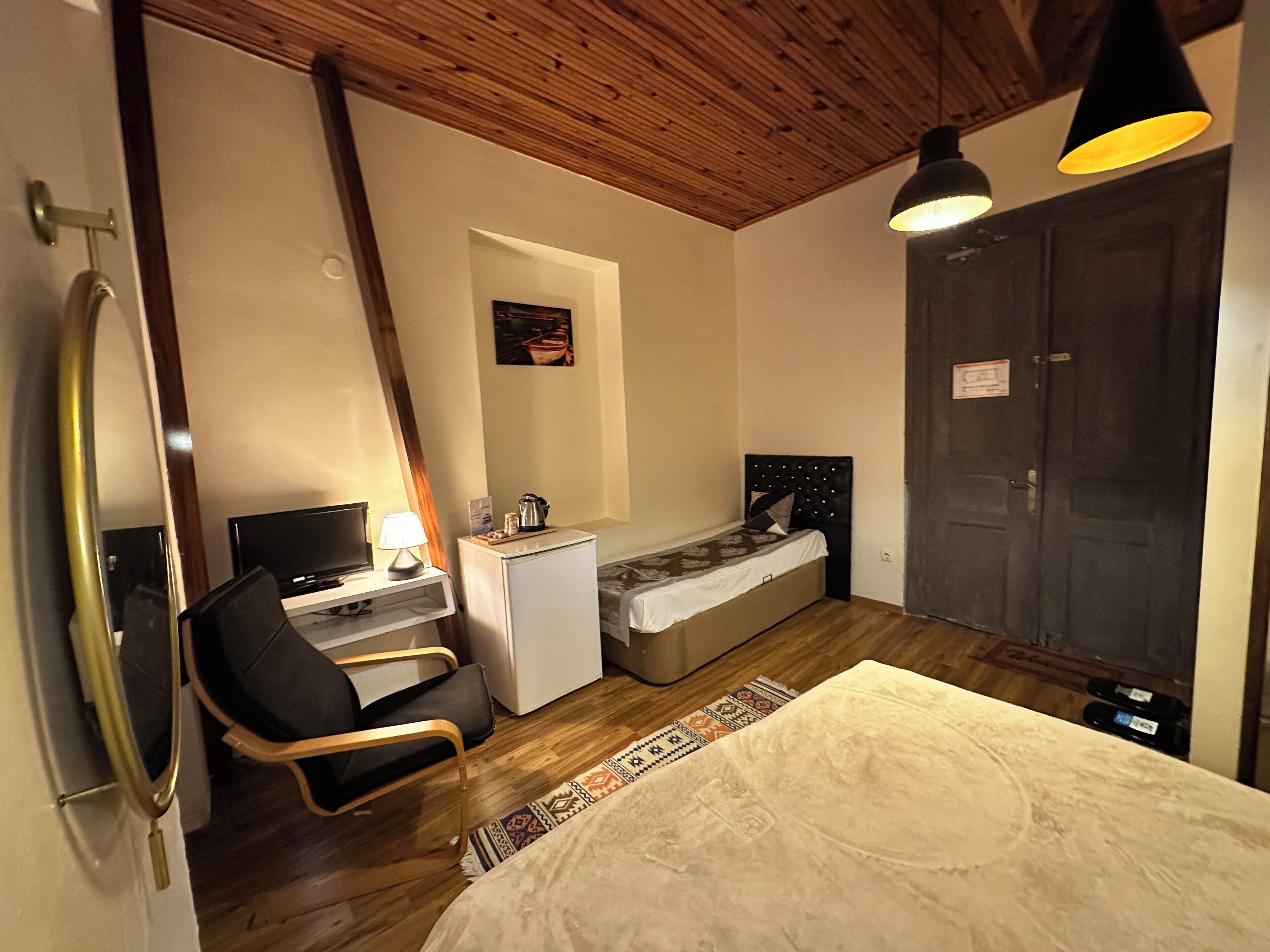 A compact bedroom with a bed, a desk with a computer, a chair, a small refrigerator, and a wardrobe.