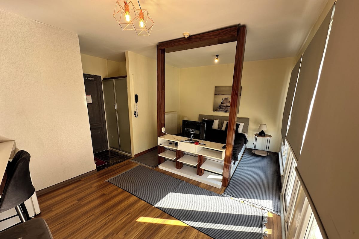 A compact hotel room with a bed, a desk, a chair, a mirror, and a wardrobe.