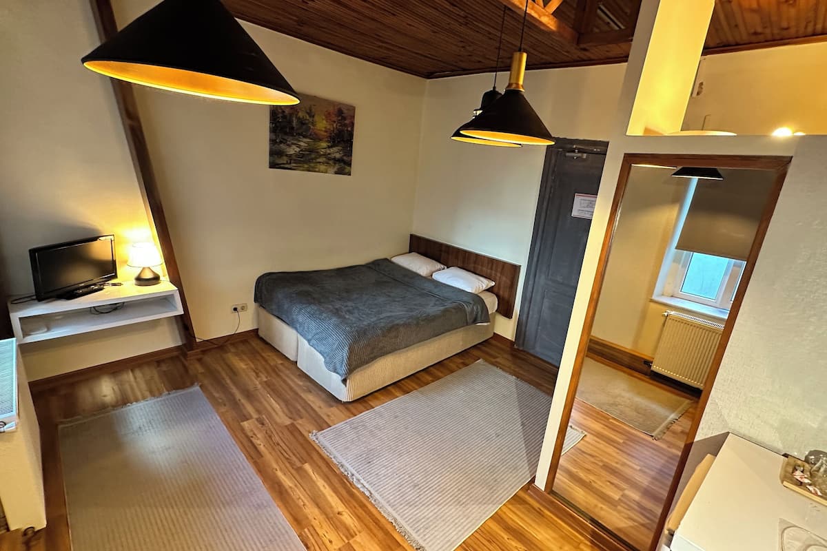 A bedroom with a bed, bedside table, lamp, and a painting on the wall.