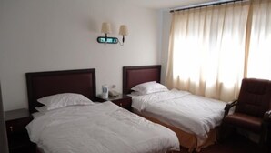 Une chambre d’hôtel avec deux lits, une table de chevet, une chaise et une lampe fixée au mur.