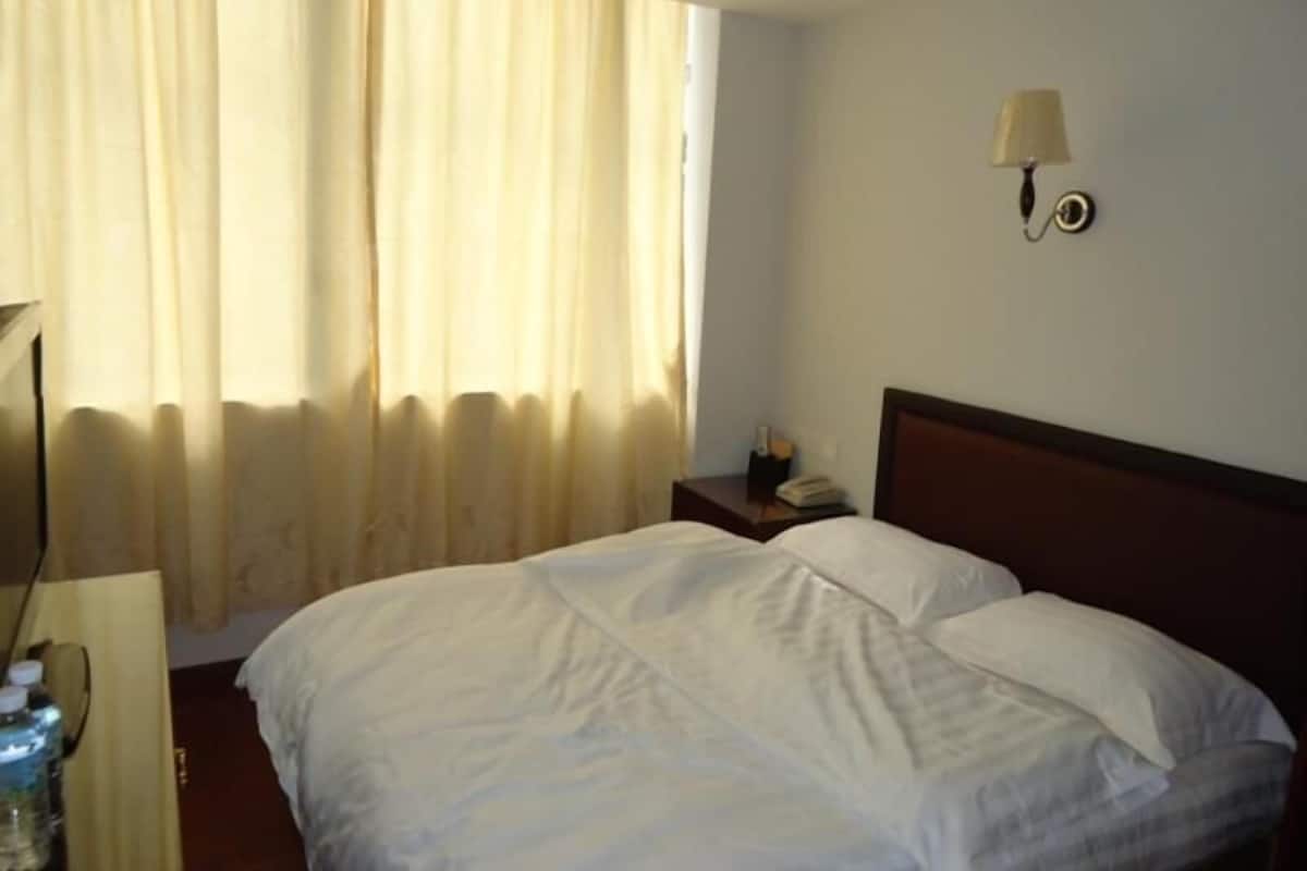 Una habitación de hotel con cama, mesita de noche, lámpara y ventana con cortinas.