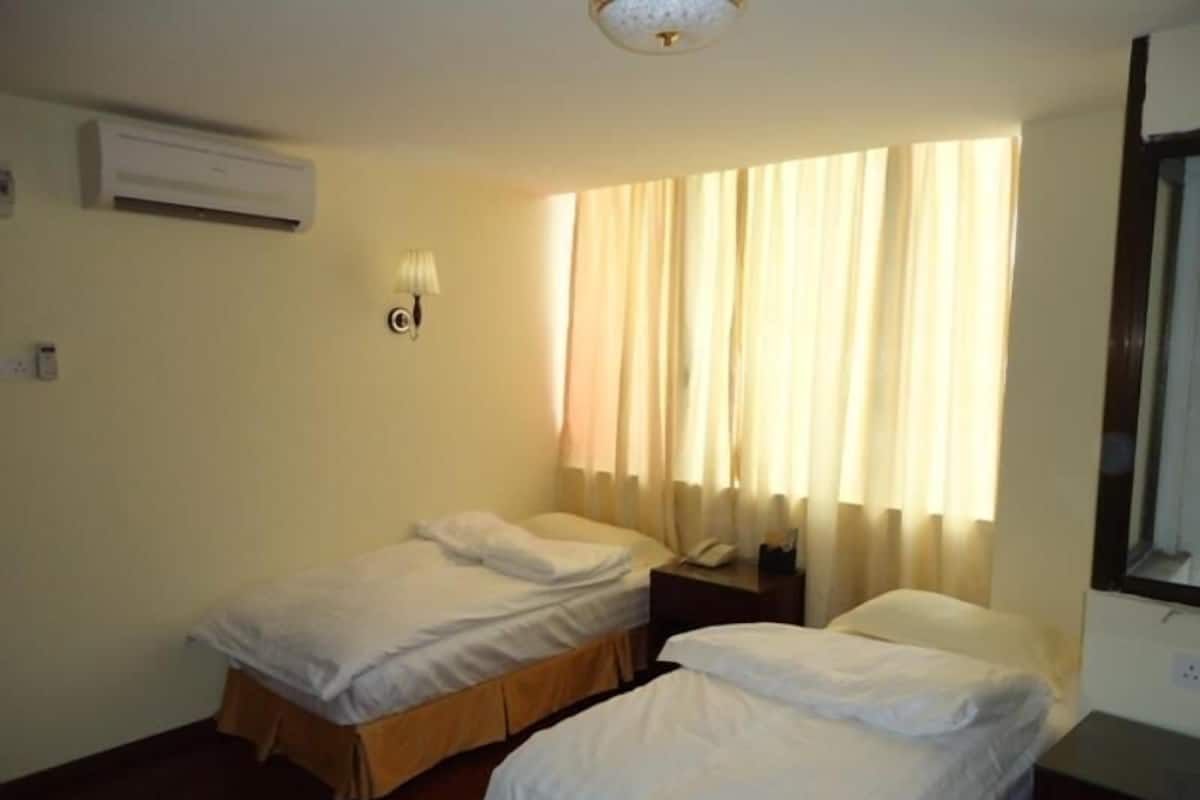Una habitación con dos camas individuales, una mesita de noche con lámpara y una ventana con cortinas.
