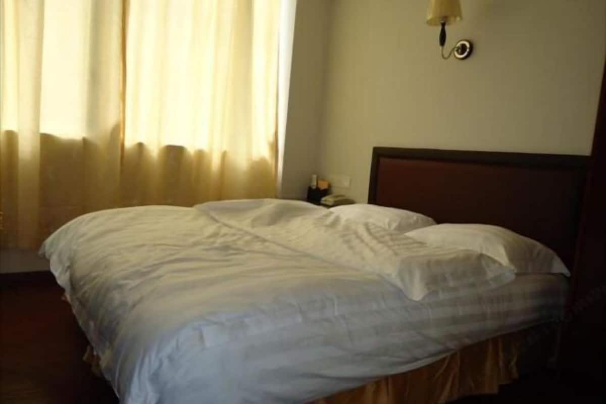 Una cama con ropa de cama blanca, una mesita de noche con lámpara y una ventana con cortinas.
