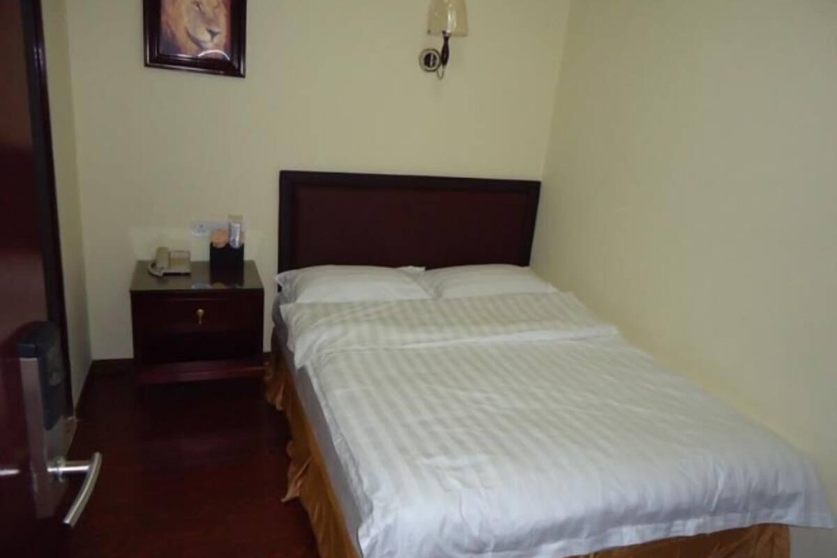 Una habitación de hotel con una cama, una mesita de noche, una lámpara y un cuadro en la pared.