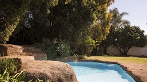 A swimming pool surrounded by large rocks and lush greenery. - Richtershuyz Guest House (Pretoria)