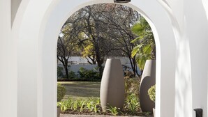 An arched corridor with a hanging light fixture, leading to an outdoor garden area with trees and a paved walkway. - Richtershuyz Guest House (Pretoria)