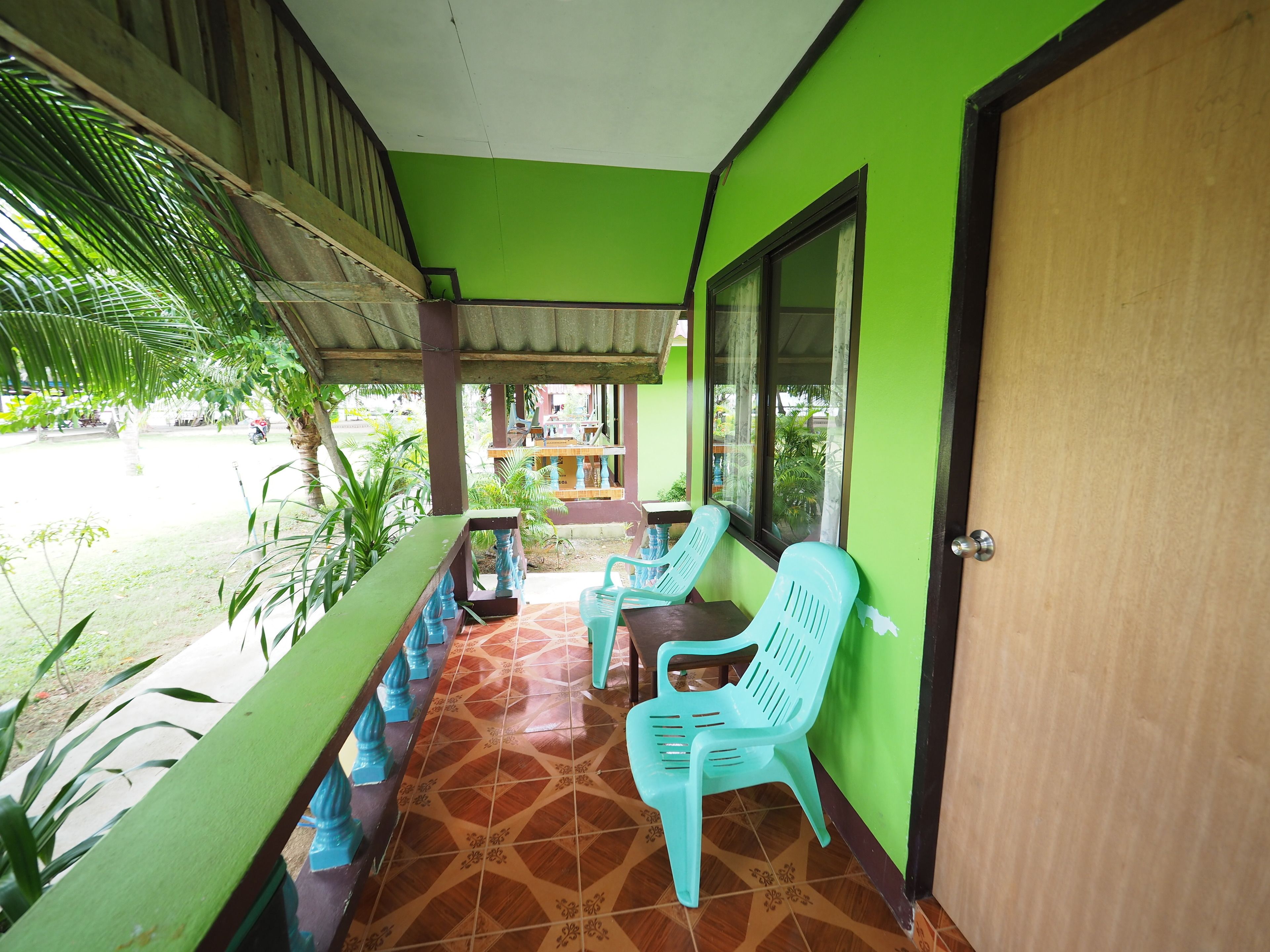 A covered balcony with two turquoise plastic chairs, a wooden door, and a tiled floor.