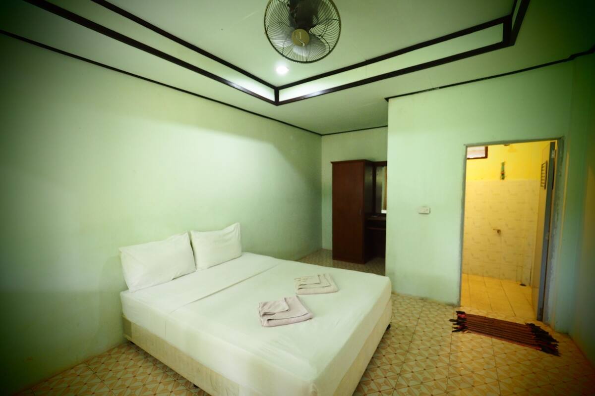 A room with a bed, a fan, a wardrobe, and a door leading to another room.
