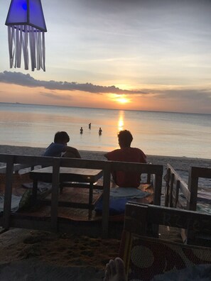 A beach scene with a sunset, people in the water, and a wooden bench area. - Lanta Darawadee Resort (Ko Lanta)