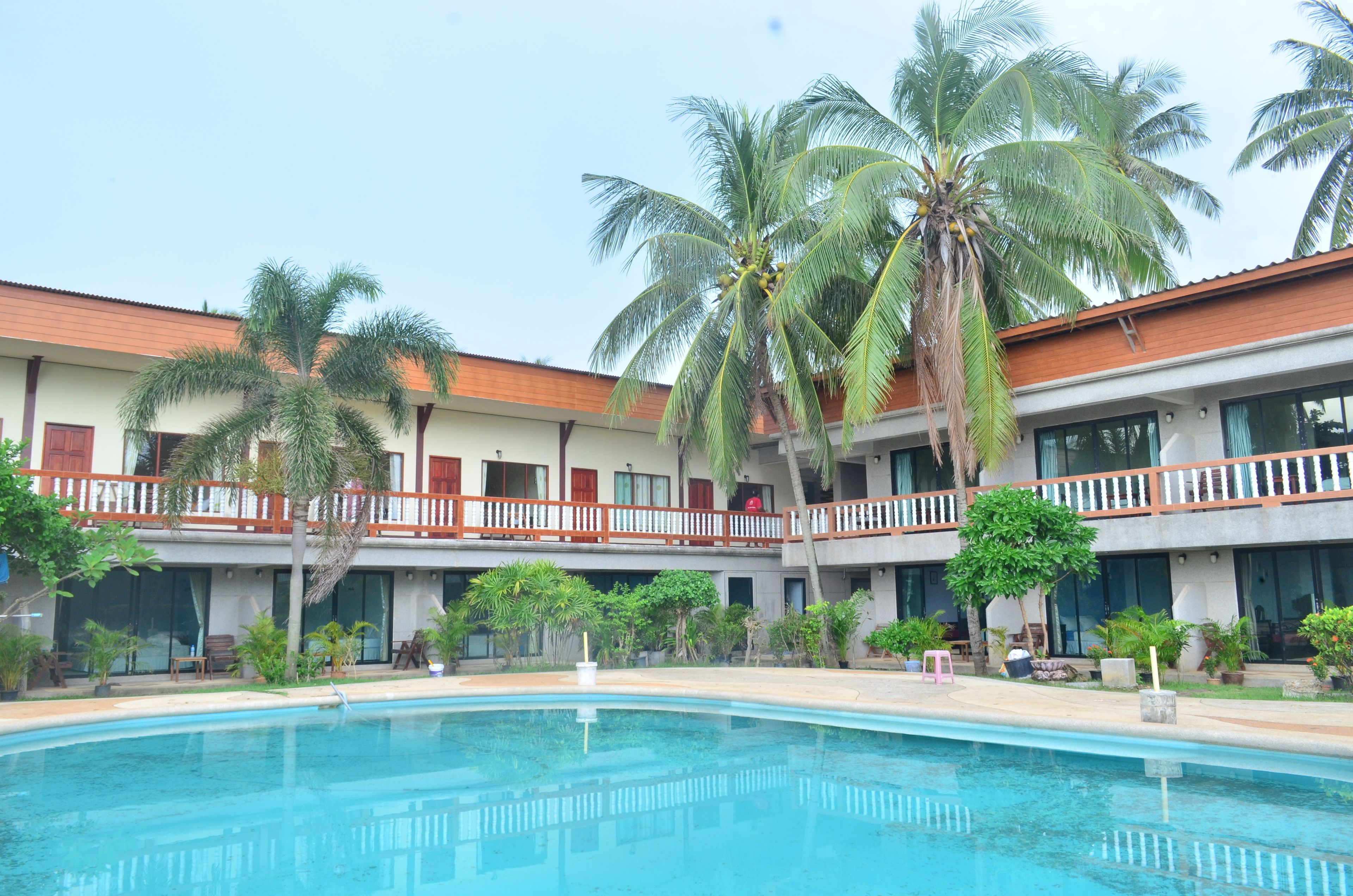 A hotel with a swimming pool, multiple balconies, and palm trees.