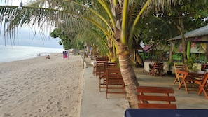 Ein Restaurant am Strand mit Holztischen und -stühlen, einer Palme und Blick auf das Meer.