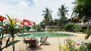 A pool area with lounge chairs, a red umbrella, and tropical plants. - Lanta Darawadee Resort (Ko Lanta)