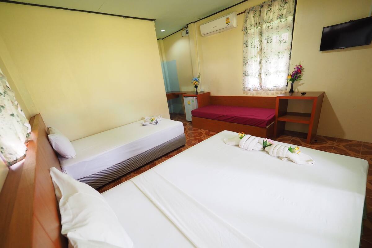 A hotel room with two beds, a wooden desk, a TV, and a small refrigerator.