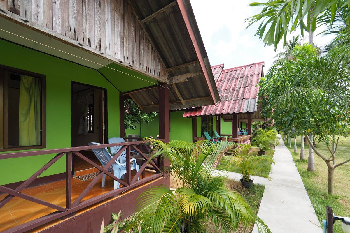 A green building with a wooden deck, outdoor seating, and a pathway lined with plants.