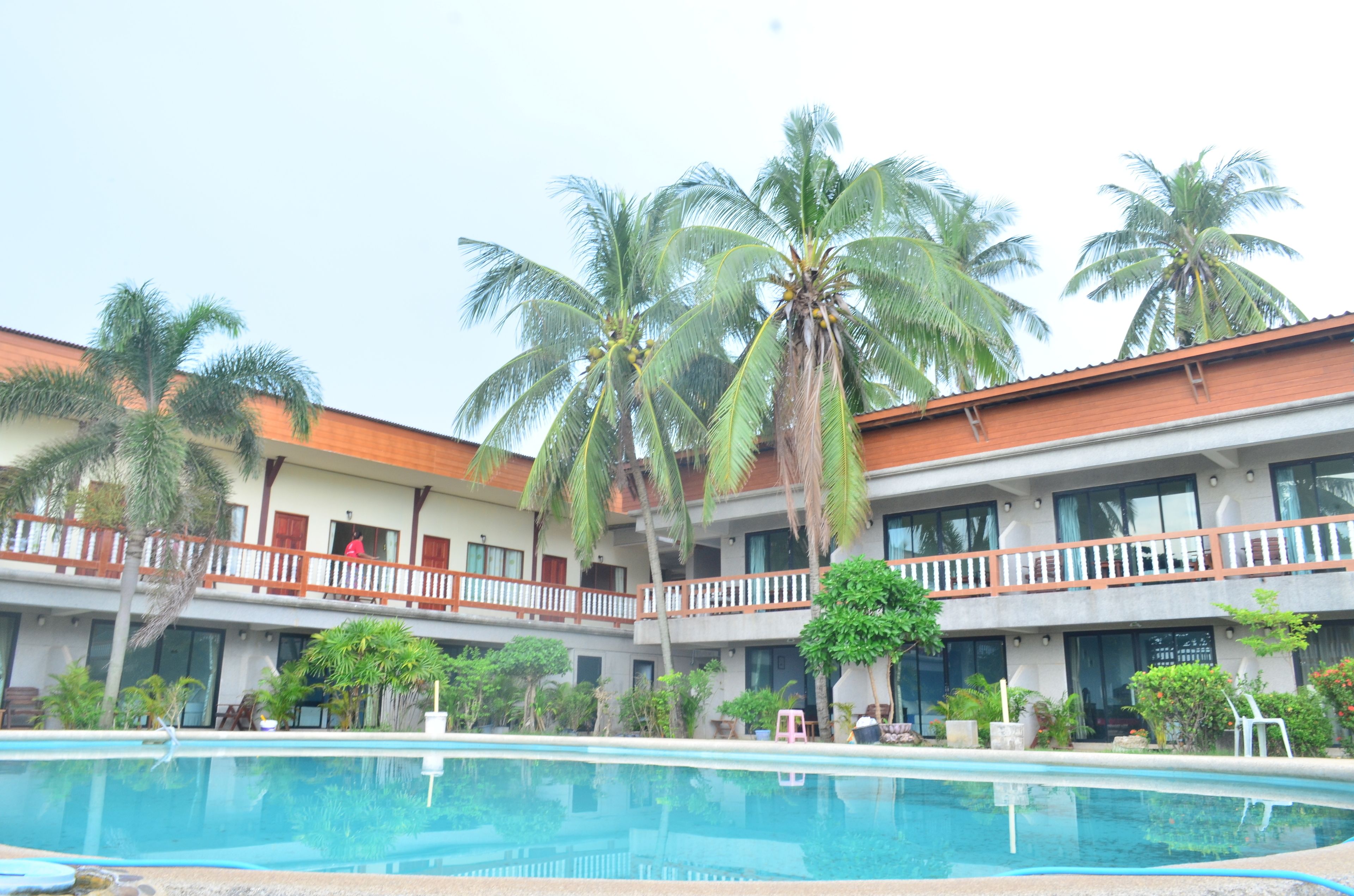 Un hotel con piscina, palmeras y un edificio de dos pisos con balcones.