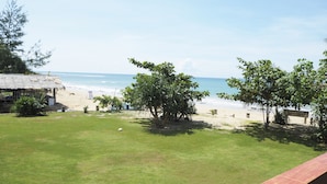 A beach view from a balcony with a grassy lawn, a thatched-roof structure, and trees. - Lanta Darawadee Resort (Ko Lanta)