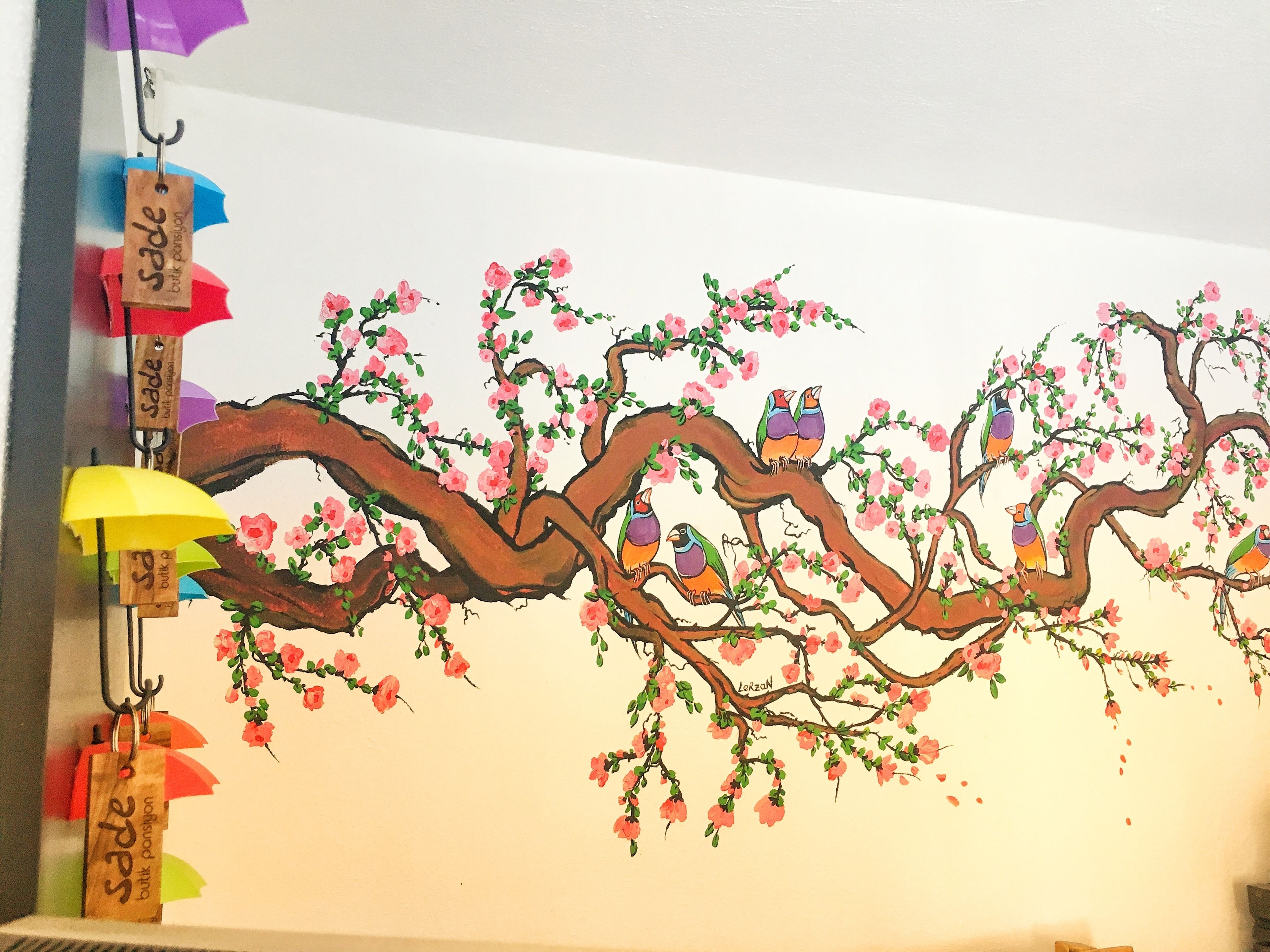 A wall with a painted tree and birds, and hanging bags with tags.