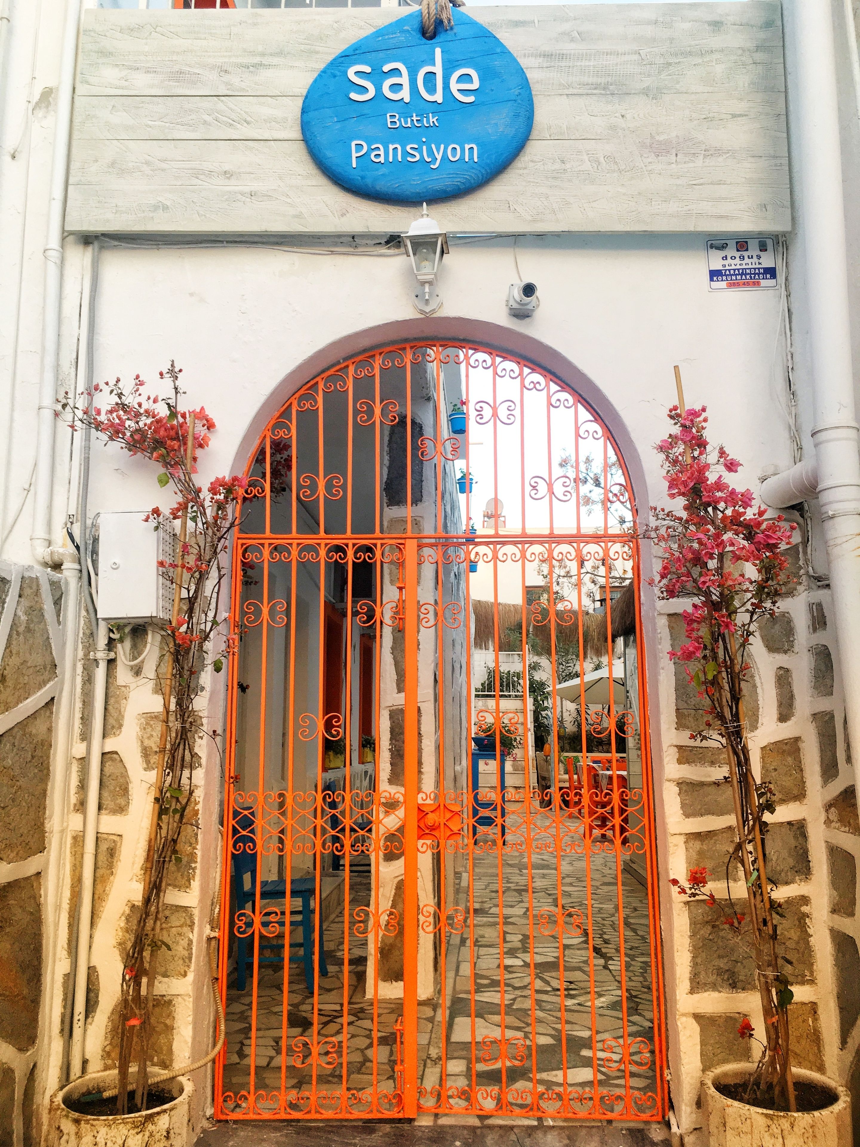 A building entrance with a blue sign reading "sade Butik Pansiyon" and an orange gate.