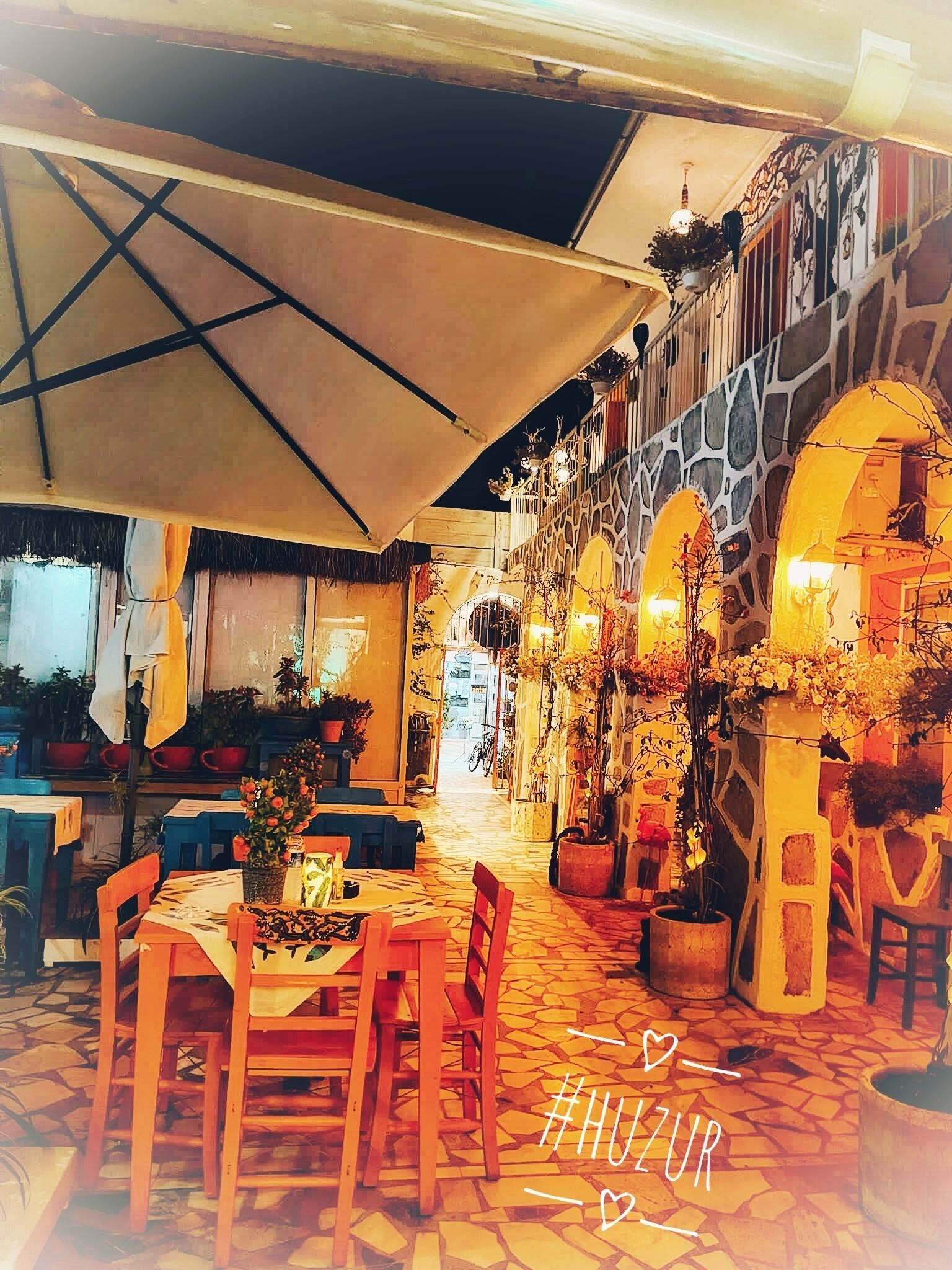 An outdoor dining area with tables and chairs, a covered walkway, and potted plants.