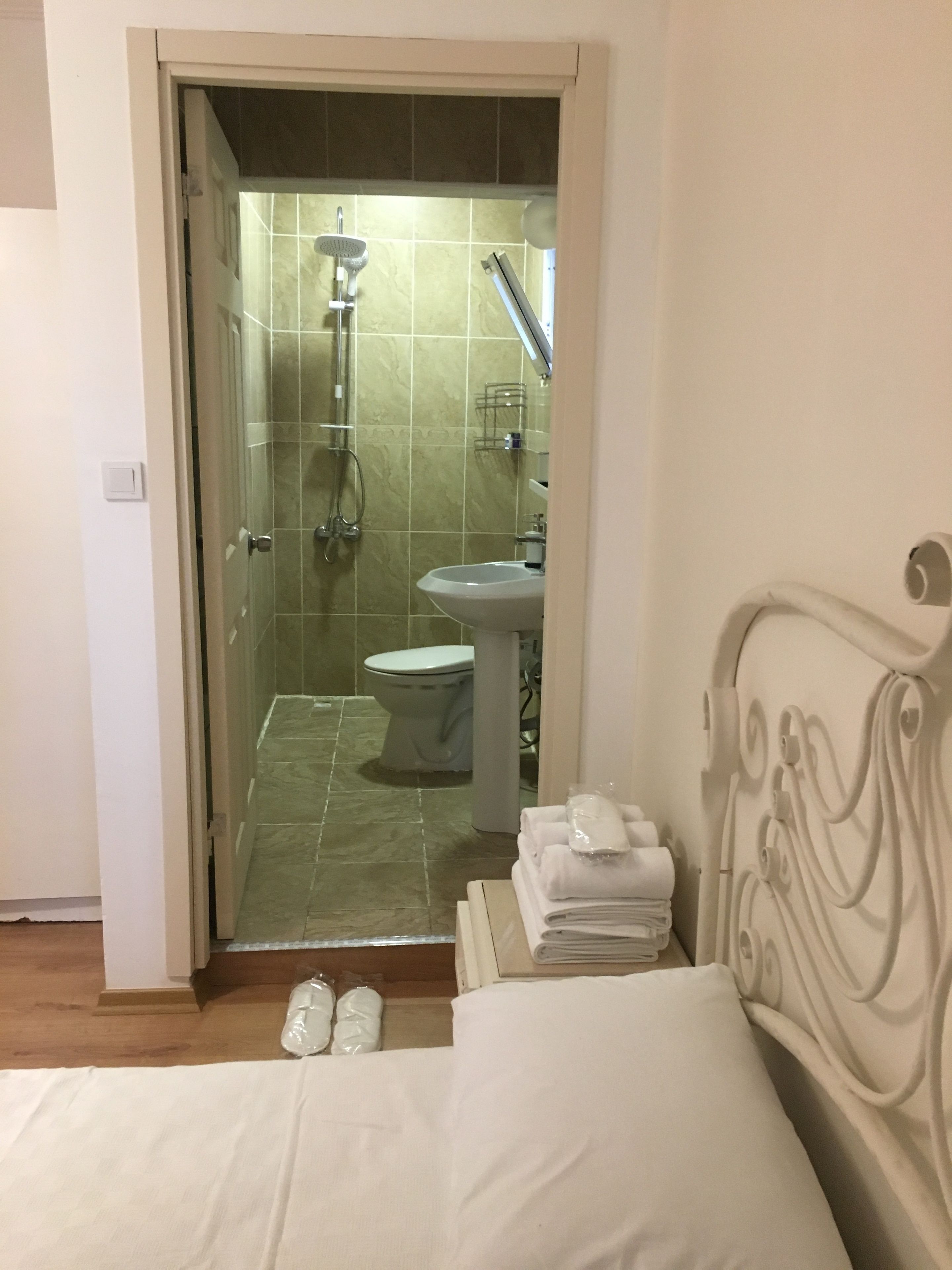 A hotel room with a bed, a bathroom visible through an open door, and a stack of towels on the bed.