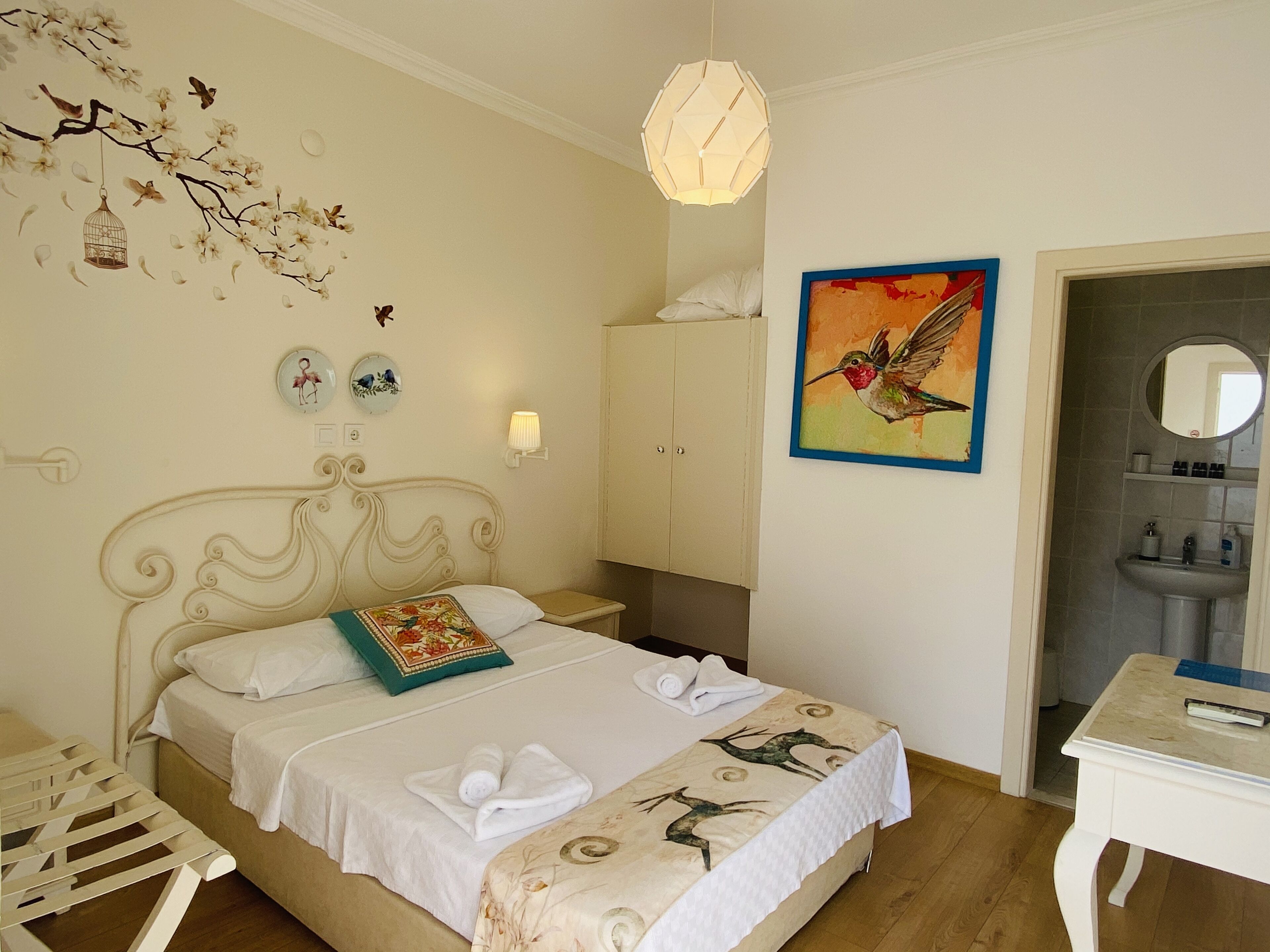 Un dormitorio con cama, mesita de noche, lámpara de pared, un cuadro, un espejo y un baño visible a través de una puerta abierta.