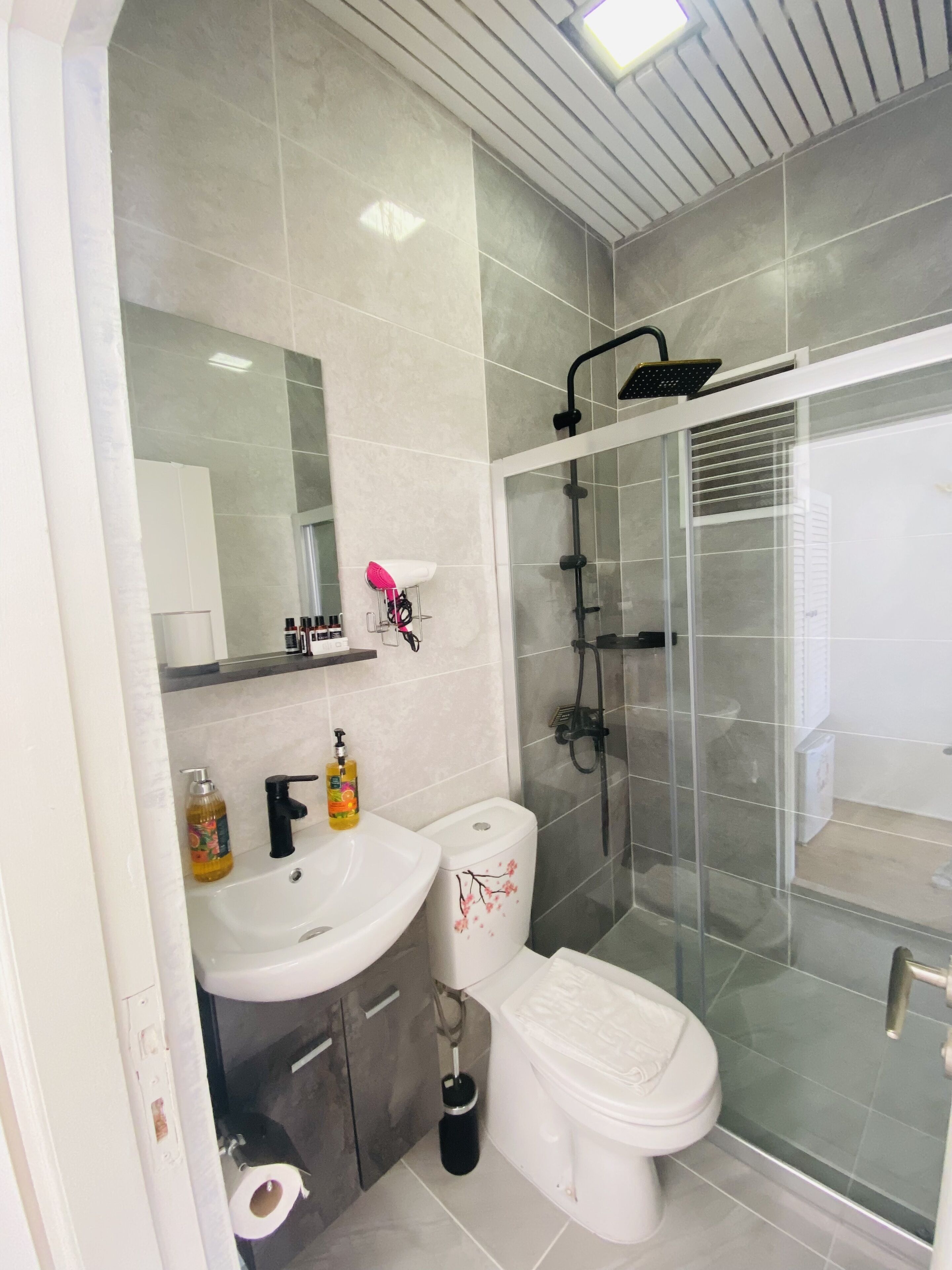 Un baño moderno con cabina de ducha de vidrio, lavamanos blanco y retrete.