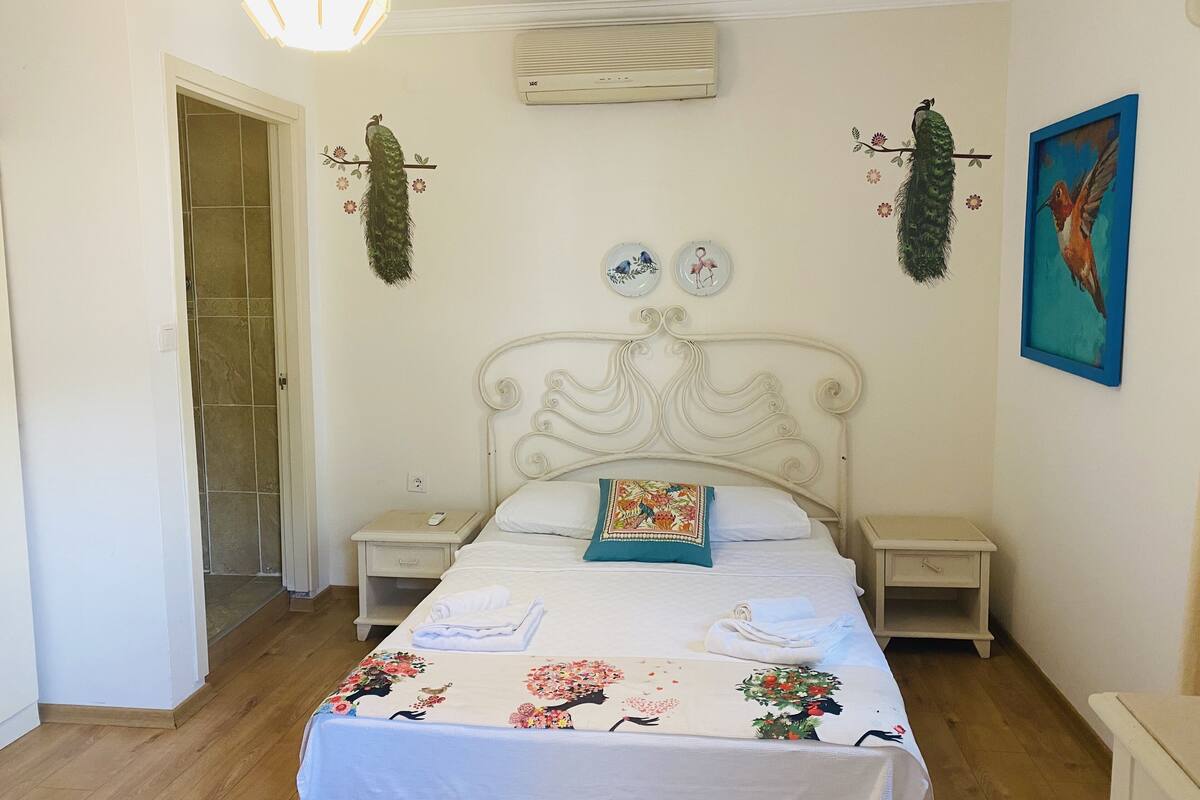 Quarto com cama, duas mesas de cabeceira, um criado-mudo, ar-condicionado fixado na parede e porta de acesso a um banheiro.