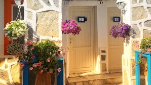 A stone building with two doors marked with numbers 3 and 4, hanging flower baskets, and a blue structure to the right. - Sade Butik Otel (Bodrum)