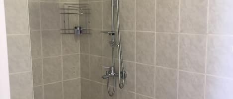 Un baño con ducha, inodoro y un pequeño estante.