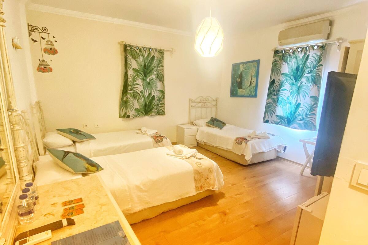 Quarto com duas camas, uma escrivaninha com cadeira, um espelho e uma janela com cortinas.