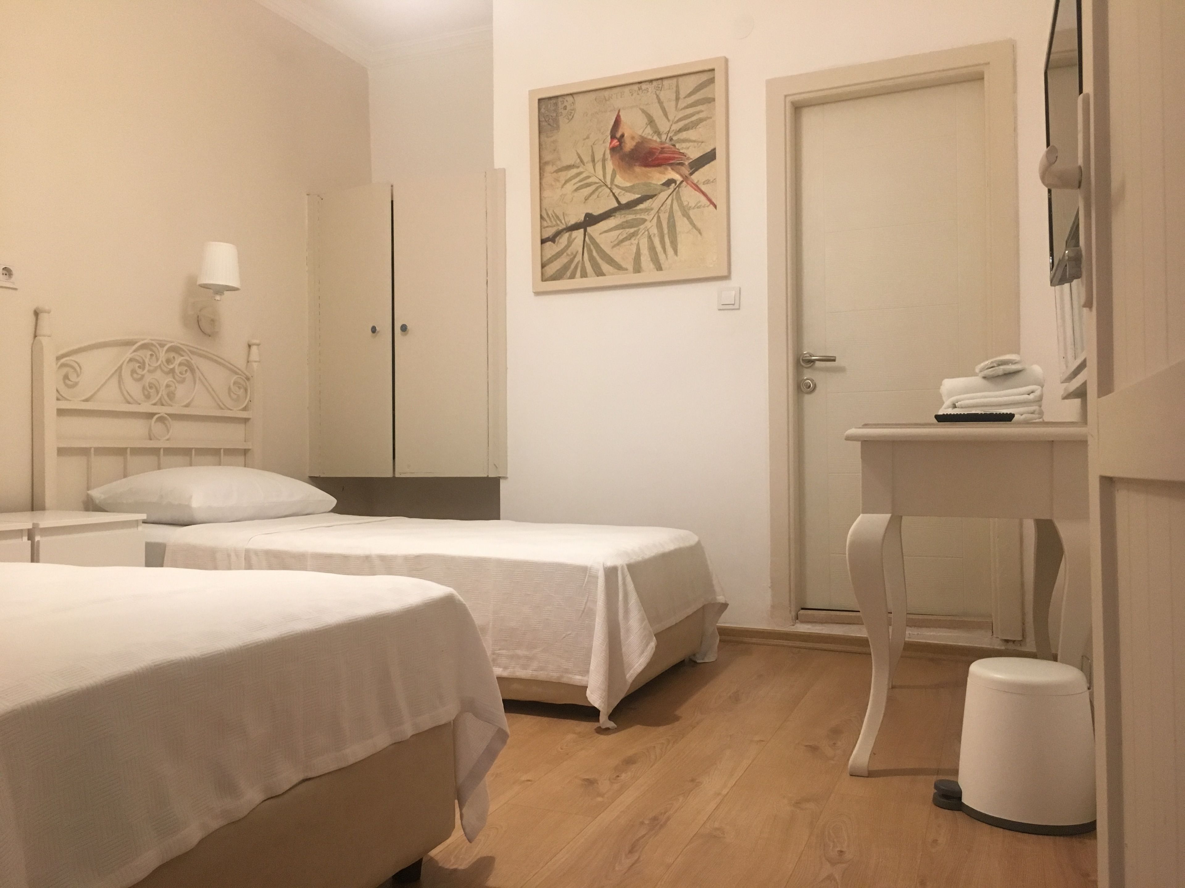 Habitación de hotel con dos camas, una mesita de noche, una pequeña mesa con un teléfono, un cesto de basura y una puerta.
