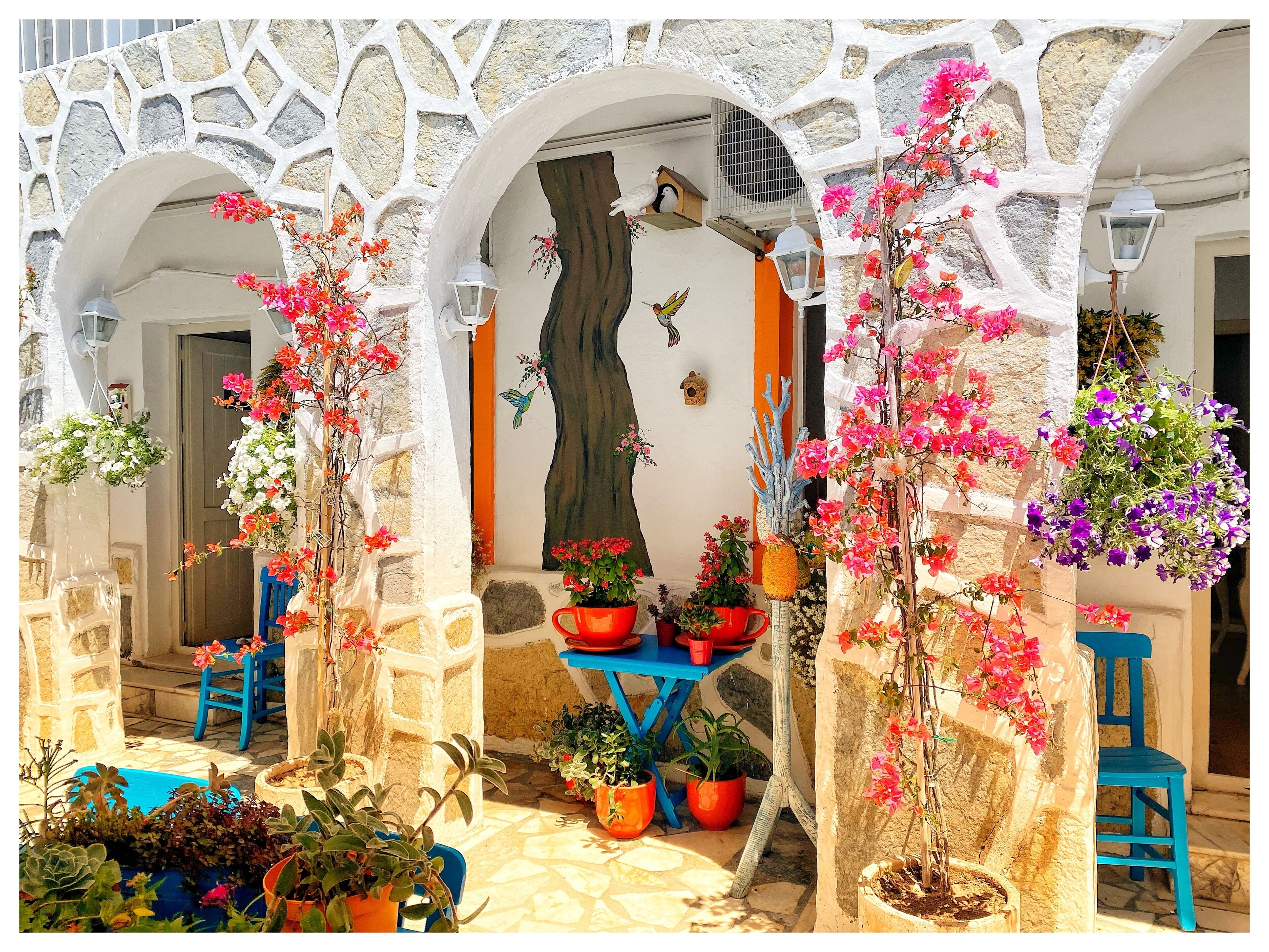 Une cour avec des murs en pierre, des plantes en pot et une table bleue.