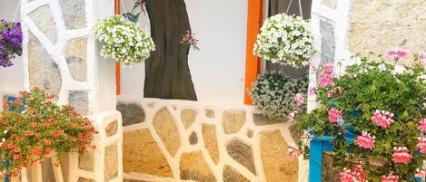 Una entrada con paredes de piedra, cestas de flores colgantes y suelo de baldosas.