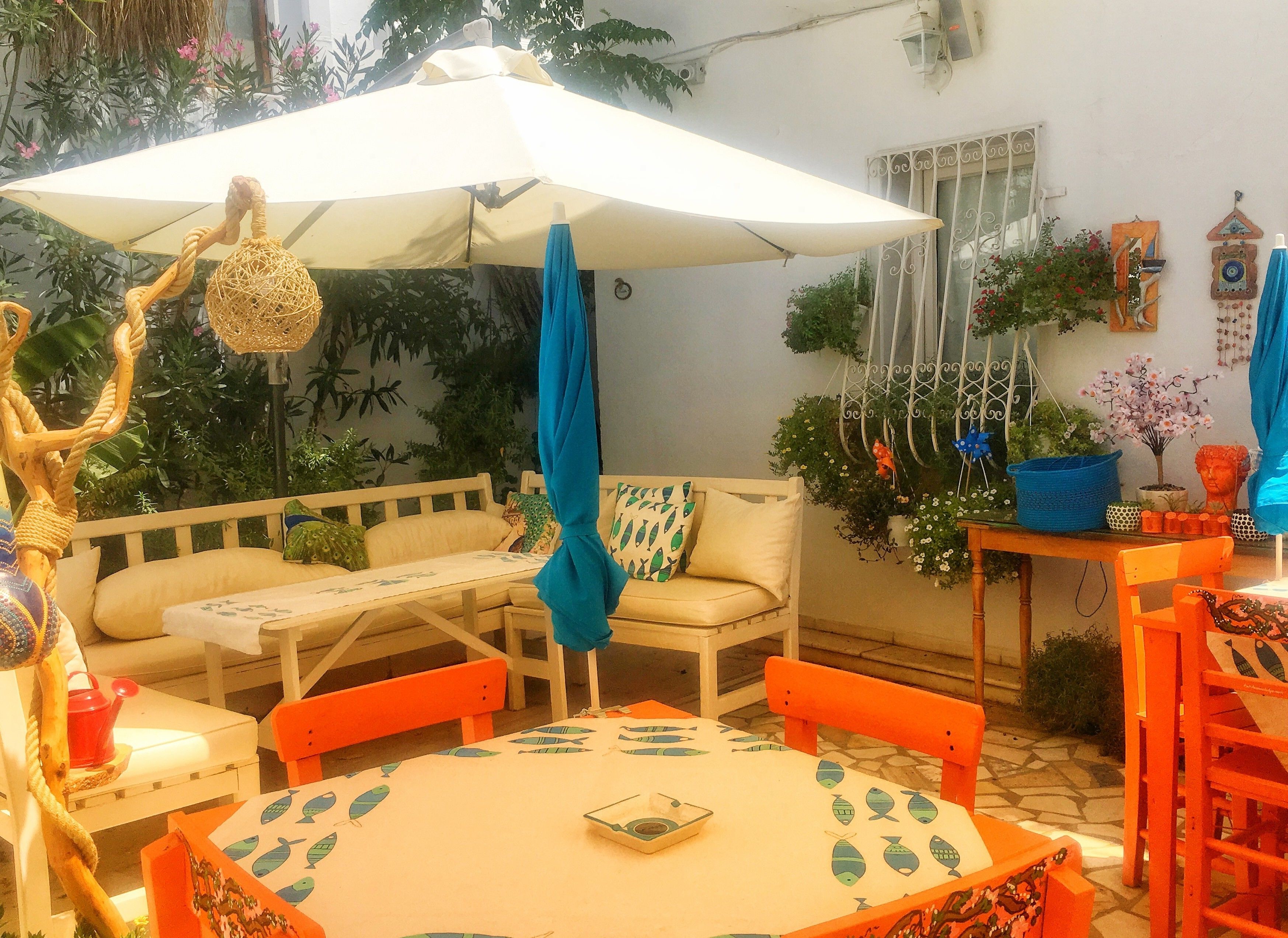 Una zona salotto esterna accogliente con un tavolo bianco, sedie arancioni e un ombrellone bianco.