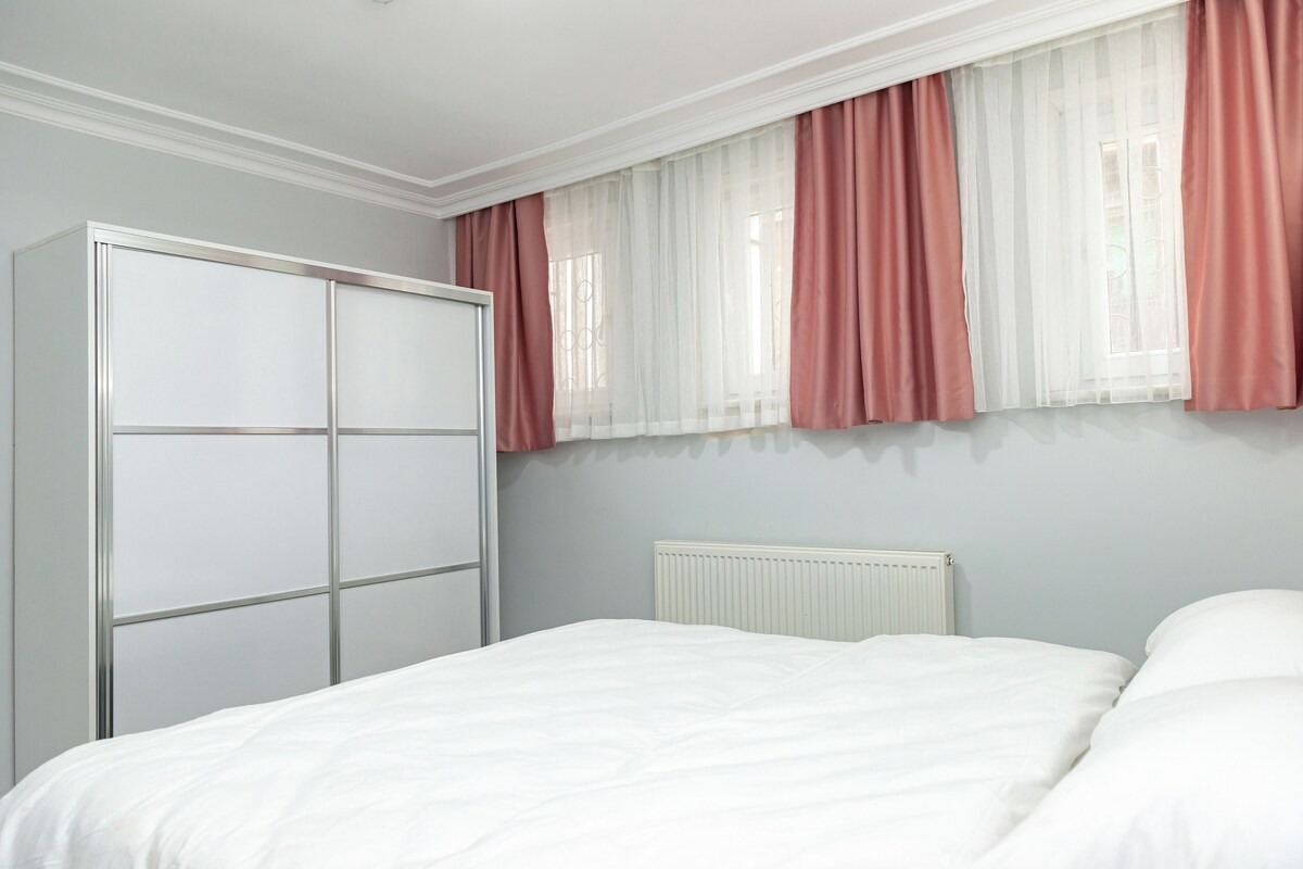 A bedroom with a bed, a wardrobe, and a window with sheer curtains.