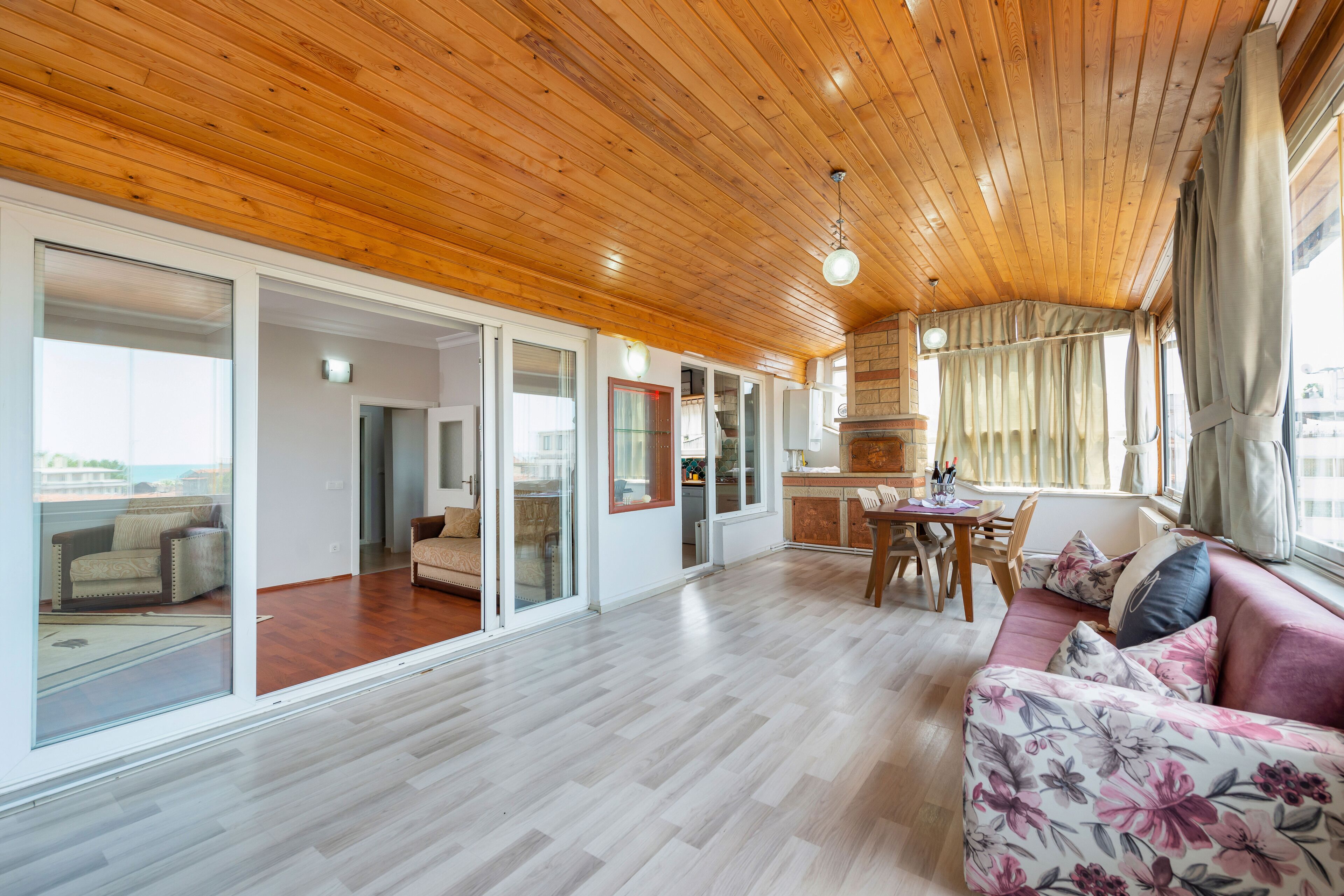 Un salón amplio con techo de madera, un sofá con tapicería floral y una zona de comedor con mesa y sillas.