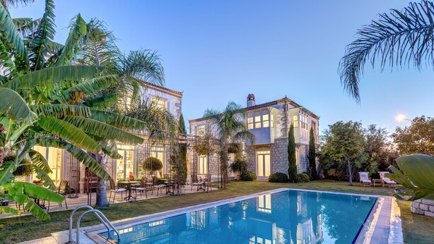 A poolside view of a two-story building with a stone facade, surrounded by lush greenery and palm trees. - Alacati Casa Bella (Cesme)