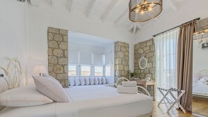 A spacious bedroom with a large bed, stone walls, a view through a window, and a wooden floor. - Alacati Casa Bella (Cesme)