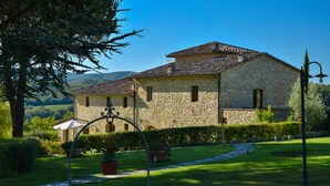 A stone building with a tiled roof, surrounded by a well-maintained garden with potted plants and a pathway. - Cavarchino B&B (Gaiole in Chianti)