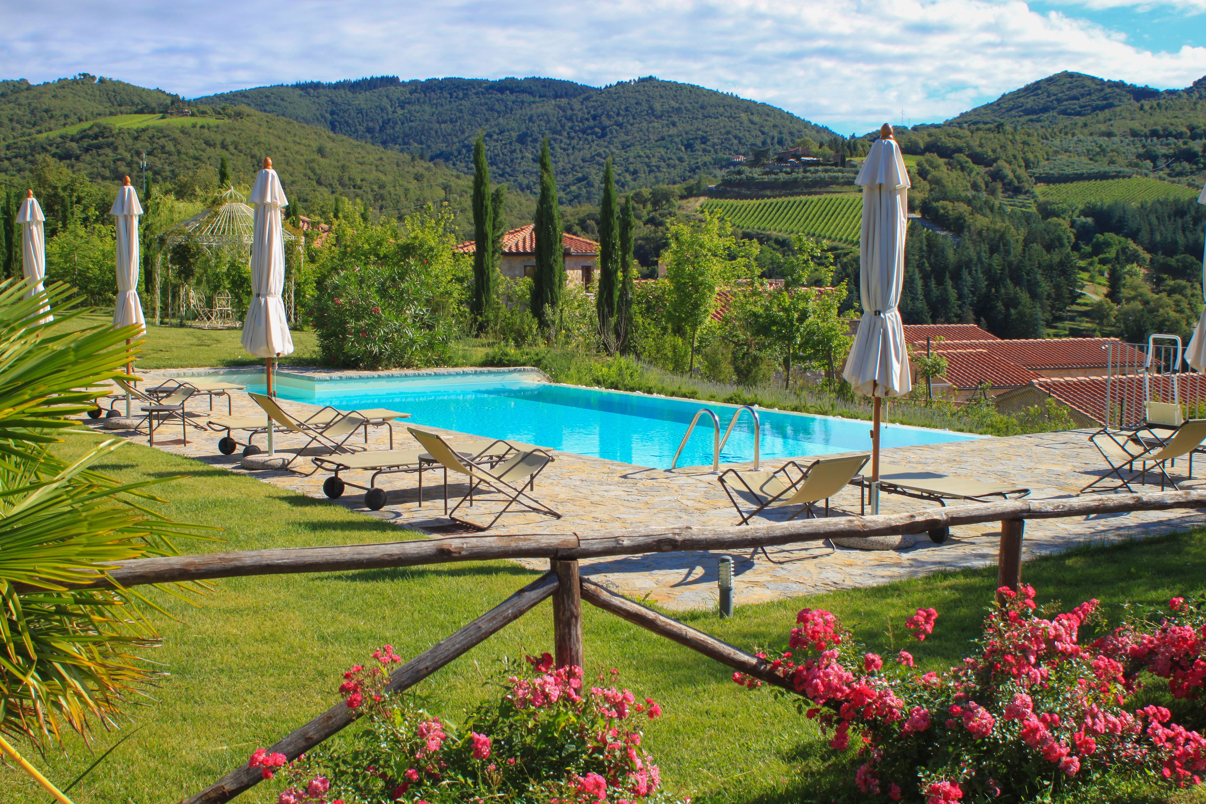 Area piscina con lettini e ombrelloni, immersa nel verde e con dolci colline sullo sfondo.