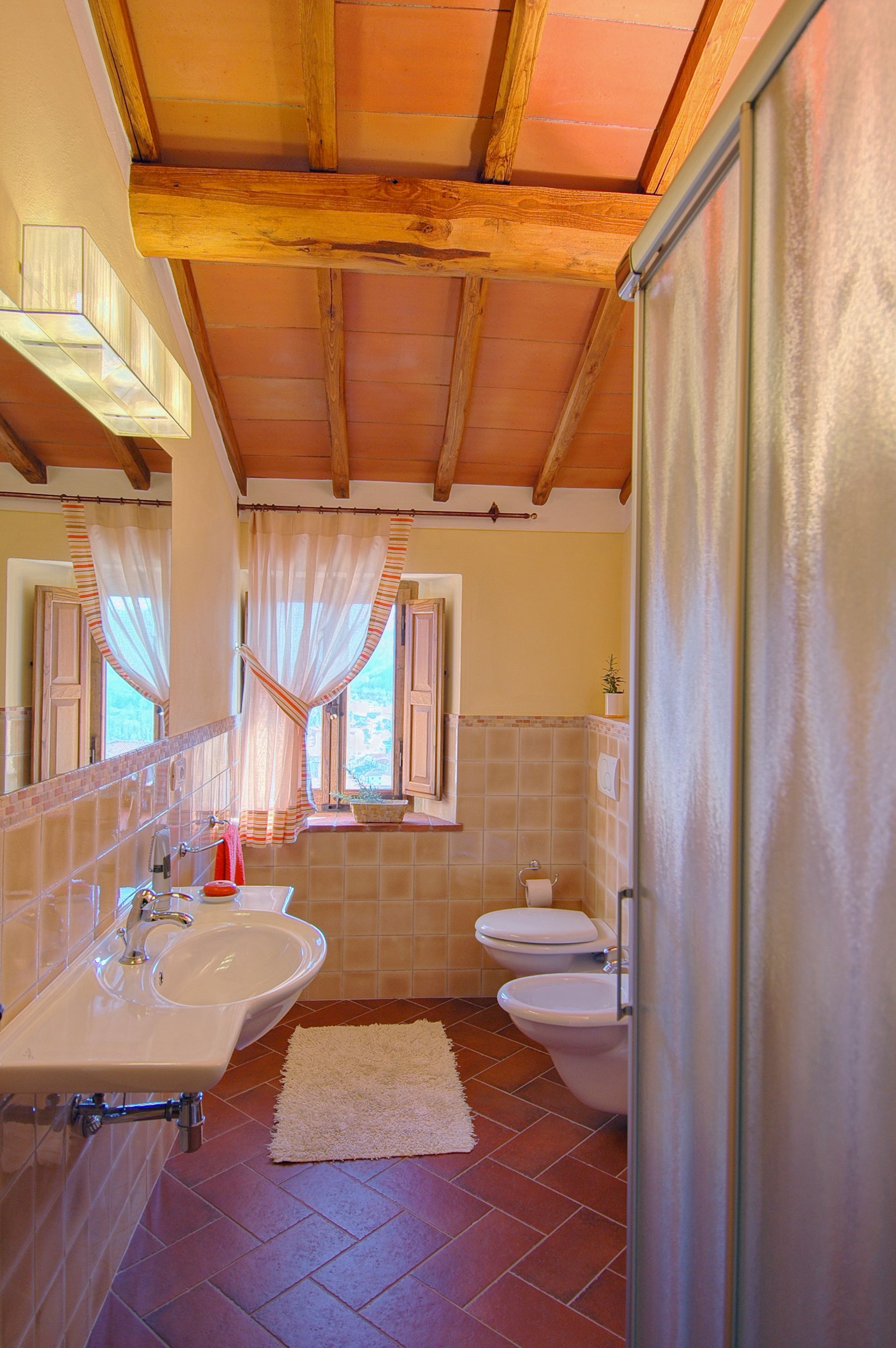 Ein Badezimmer mit Holzboden, einem Waschbecken, einer Toilette und einem Fenster mit Vorhängen.