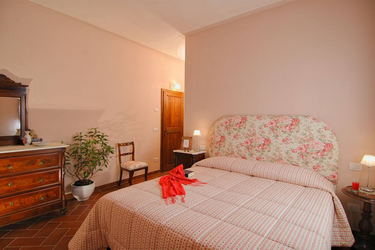 A bedroom with a bed, dresser, chair, potted plant, and a door.
