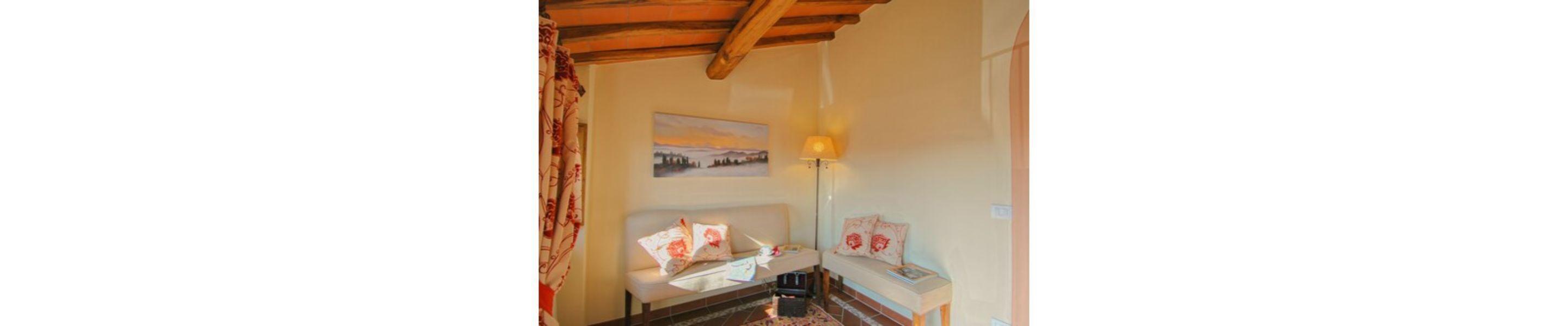 Une pièce chaleureuse avec un plafond en bois, un lit recouvert d’une literie à motifs floraux, une table de chevet avec une lampe et un tableau accroché au mur.