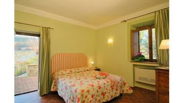 Un dormitorio con cama, una ventana con cortinas, una mesita de noche y una lámpara.