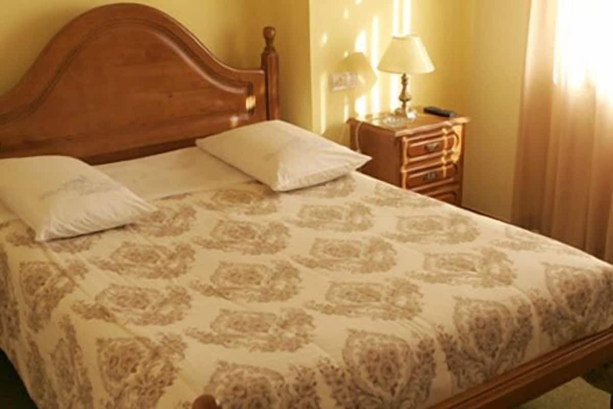 A neatly made bed with a patterned bedspread, a wooden headboard, and a bedside table with a lamp.
