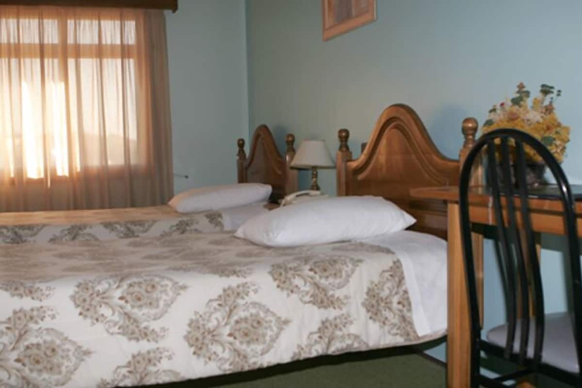 A bedroom with a bed, a wooden headboard, a chair, and a table with a lamp.
