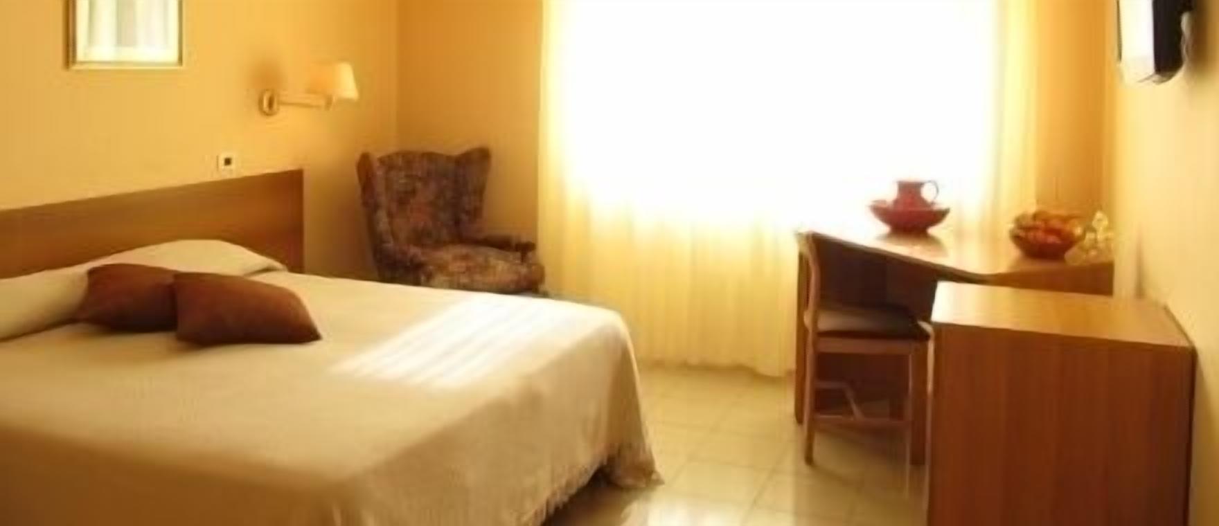 Una habitación de hotel con una cama, una silla, un escritorio y un ventanal con cortinas.