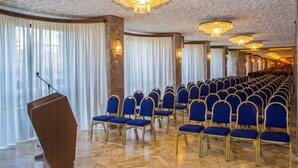 Un salón de conferencias con filas de sillas azules, un atril de madera y candelabros.