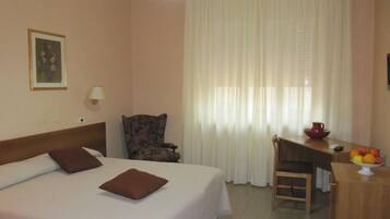 A hotel room with a bed, a desk, a chair, a lamp, and a painting on the wall.